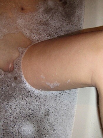 A pair of long legs and bare knees submerged in a bubble bath, water lapping at the flesh.