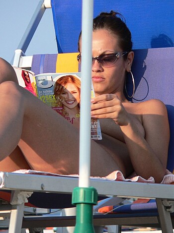 """
A titty-assed bitch chillin' sans shirt on some beach furniture, squinting in sunnies as she peruses a mag.
""