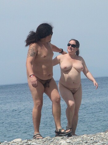 A guy and a chick with no clothes on are getting their dicks out by the shore.