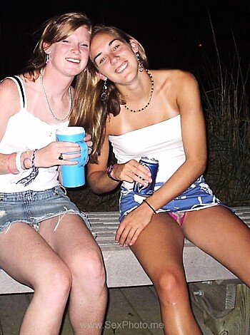 Here are two chicks with no tops on, sipping on some booze while sitting on a bench.