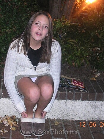 A naked chick is taking a shit in the dark while wearing a jacket and some shorts.