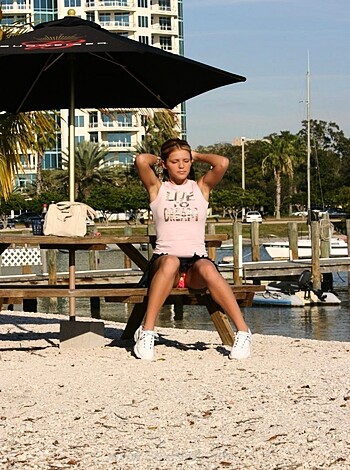 Here's a vulgar description of the image: "Young slutty bitch poses by the fuckin' lake in her pussy-pink shirt."