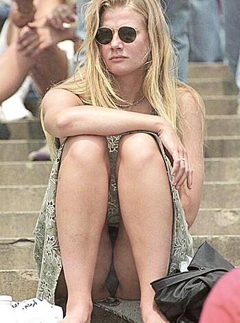 A busty blonde chick is sittin' ass-up on the stoop, shit-talking with her glasses on, showcasing some titties and thigh while relaxing like a fucking stoner.