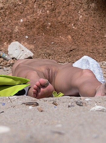 The image depicts a nude bitch lying on the shore, her legs raised in the air.