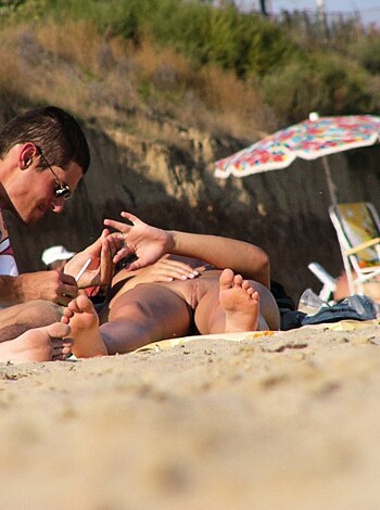 "Check out this fuckin' pic of two dudes chillin' on the beach while one bro gives another bro a foot rub. The guy getting massaged has his ass in the air with his legs up in the air, sporting some sexy shorts and shades."