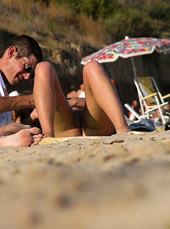 A pair of dudes are chillin’ on the beach with one dude shavin’ off his buddy’s leg hair while they’re both butt naked.