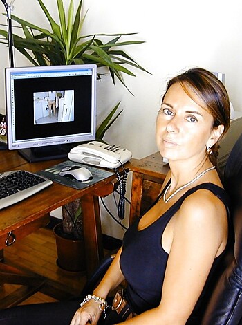 A naked chick sits on a desk with some bling-bling on her arm and neck.
