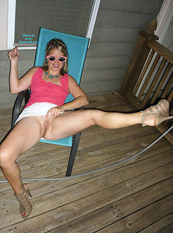 A nude chick, with a pink top on, smokes a ciggie, flashes her twat.