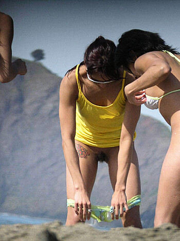 Look at these two sluts in their sexy bathing suits, all tanned and fit, standing on the beach like they own it. One bitch is wearing a pink thong while the other is rockin' a yellow bra. Fuck knows what the fuck they're staring at each other for; probably just trying to out-slut one another. The sun's beating down on their tits, making them shine like diamonds. This photo's so hot I might need to jerk off in front of it later.