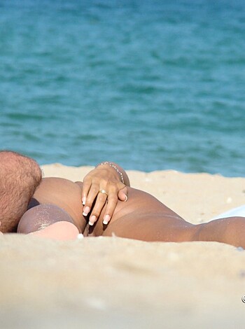 This motherfucking picture shows a fucking naked pair of sunbathing assholes on the goddamn shoreline, with no clothes covering their dickheads and pussies.