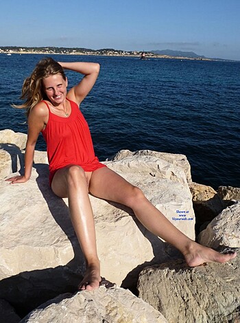 A bitch in a sexy red dress is sunbathing nude assed on some fuckin' rocks by the beach while smiling for the camera like a goddamn dumb cunt.