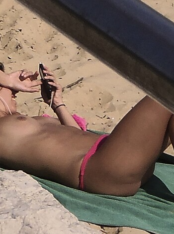 A naked chick in a bikini lying on the sandy shore, with her tits hanging out, checking her fucking iPhone.