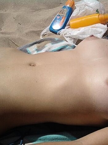 The image shows a f*cking hot bitch lying on a beach towel, completely nude except for her tits that are dangling in the open air.
