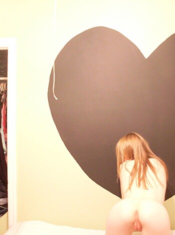 A bitch is knelt nude with a heart shaped adhesive label stuck on the fucking wall supporting her back.