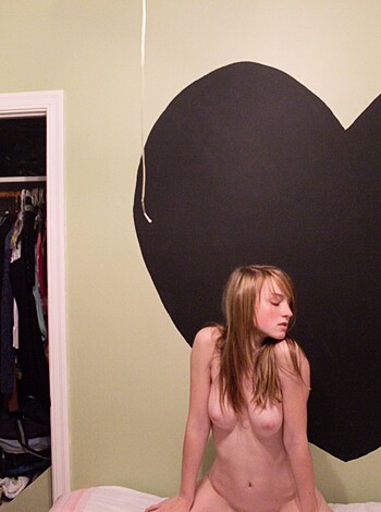 Here's the fucking image of a hot ass bitch with big tits, sprawled out nude across a fucking mattress while fucking posing for a photograph next to some goddamn romantic fucking black heart poster that's hanging on the wall behind her.