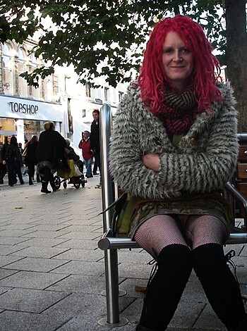 A bitch is sitting on a bench with a tight ass fucking dress on, wearing some goddamn fucking hose on her legs.