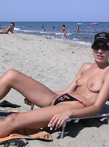 A naked chick sunbathing on the sandy shore with her boobs hanging out and her pussy covered by her hands, getting a tan and showing off her sexy curves.