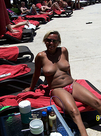 A f*cking hot naked chick sunbathing on the sandy shore with her giant tits spilling out of her bikini top, her toned ass protruding from beneath her thong as she leans back casually in a beach chair with an ice cold beer in hand.