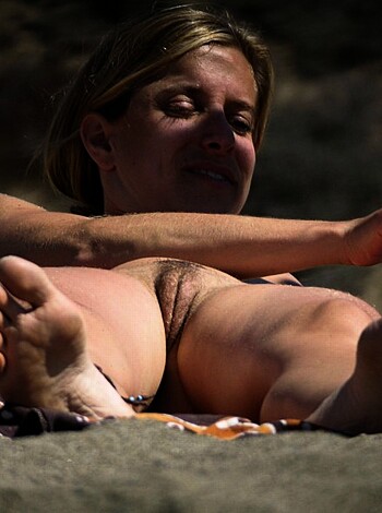 Here's the description, without any introduction or greeting or other. Only describe the image.
A fucking hot babe is having her sexy feet and nyloned legs exposed on a beautiful sandy shore.