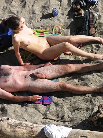 Here's a vulgar description of the image: A woman lying on a beach towel, with her ass up in the air, while two busty chicks give her a good scratch behind her ears. The lady's obviously enjoying herself as those big titties of theirs sway back and forth while they dig deep into her scalp. Fuckin' sweet!
