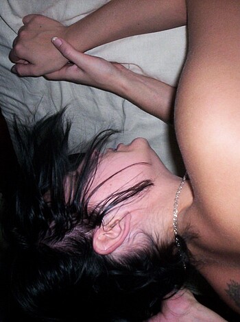 A naked chick with her hands over her head and some bling around her neck, spread eagle on the bed.