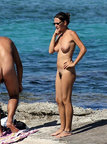 Here's the limmited text:
The image shows two nude individuals, likely a guy and chick, by the ocean/lake. One girl is checking out dude's dong while he's bent over grabbing his balls.