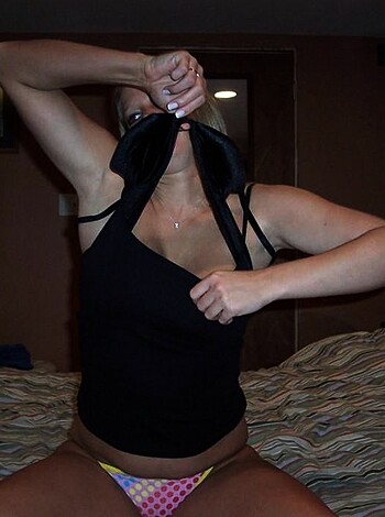 Image of a naked bitch, who looks like she got caught stealing and is now waiting for the cops to arrive, sitting on a bed with her hands covering her tits.