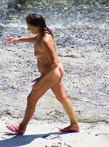 A nude chick sunbathing on the sandy shore.