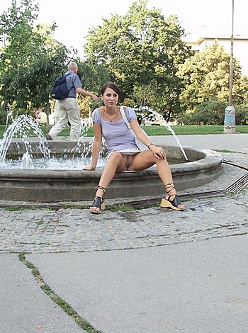 A bitch sits by a fucking fountain with her pussy on display, dressed in some gray shit and some shorts.