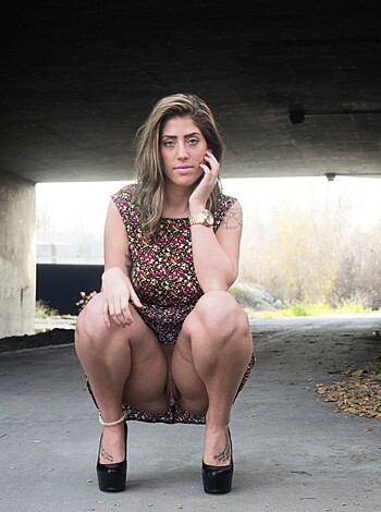 A fucking bitch with her legs spread wide open is lying down on the grass while wearing a skirt and high heels, gazing at the sky in a suggestive manner.