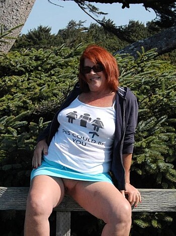 A hot chick with red hair is chilling on a bench, sporting a sweet blue shirt.