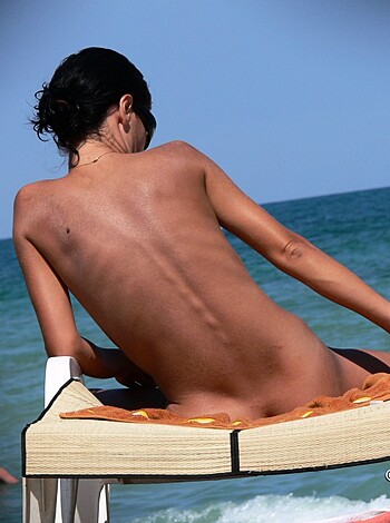 A busty babe sits on her ass cheeks on a beach chair with her titties out, exposing herself to anyone who's lucky enough to be in sight.