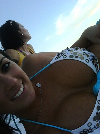 A scantily clad babe wearing a skimpy bikini sips on a frosty brew while lying on her ass and sporting a big smile for the camera.