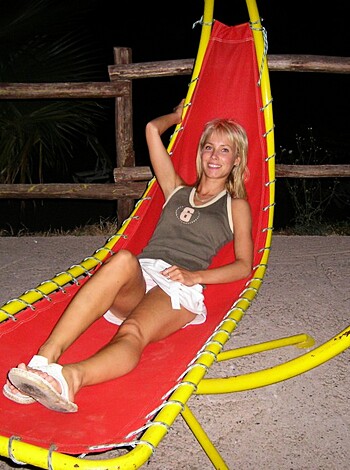 A chick with cherry red and white bikini briefs lounging on a sunny, canary yellow outdoor chaise lounge.