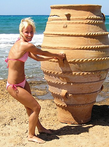 Busty blonde chick in a bikini grinding her ass on an old ceramic pot while laying on some sandy shore, trying to act classy but just looking like a dumb slut who's probably got herpes from fucking too many guys.