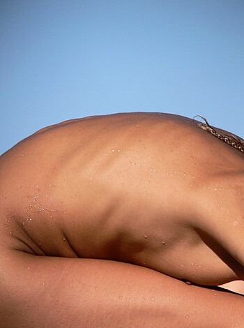 The chocolate-colored woman with curly locks kneels down on her haunches while placing her palms together in a prayer-like position.
