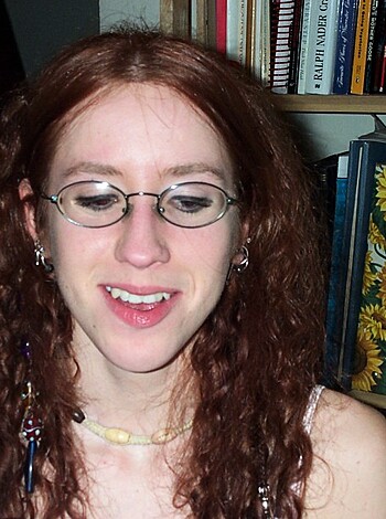 "Here's a hot chick with huge tits and a sexy smile who's not afraid to show off her cleavage in a tight white tee while wearing some red bitchin' beads around her neck, baby! You wanna take a closer look at those glasses? Fuck yeah, they make her look smart as fuck too."