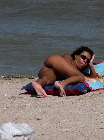 A chick lies down with no bra and briefs, sprawled out on her ass on a towel, donning sunnies.