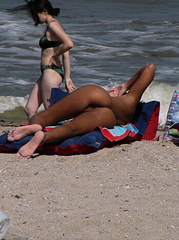A naked chick lying on her back on a sandy shore while showing off her juicy tits and ass in a tight-ass bikini.