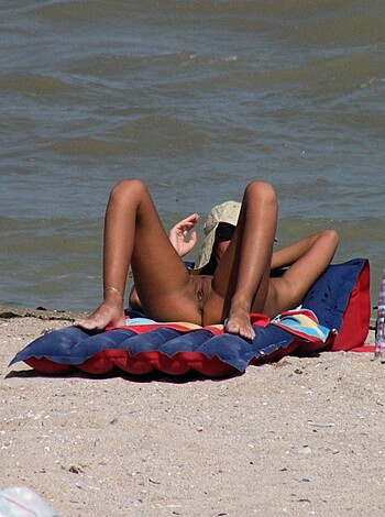 Image of naked person lying on a fucking towel on the sandy shit with their ass in the air while enjoying the sun and probably waiting for someone to come suck their cock or pussy.