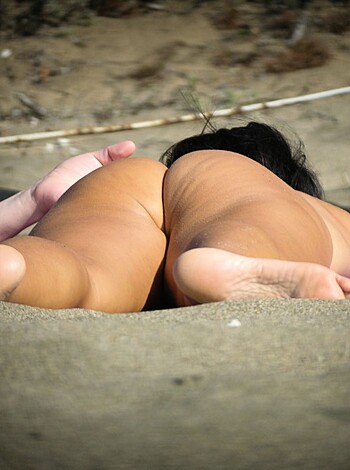 A topless babe lies on the beach sand with her legs splayed open wide, while some dude's hands are in between her thighs.