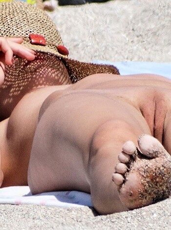 This fucking picture shows some hot bitch lounging on the sandy shore with her toes poking out from under a sunhat, catching rays like a goddamn suntanned goddess.