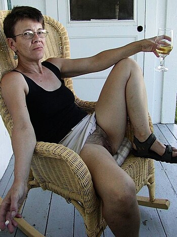 Here's the vulgar caption for the image of a hot chick sippin' on some wine while sittin' in some shitty ass wicker chair, her tits lookin' like they're about to spill outta that tight black tank top she got on.