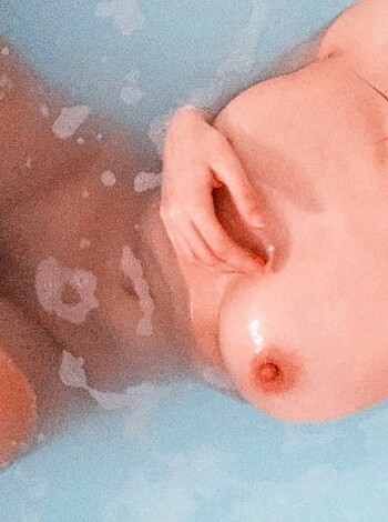 "Take a gander at this photo of a naked chick perched on the edge of a tub, leanin' over to see her reflection in the water while she casually props up her tits on her thighs."