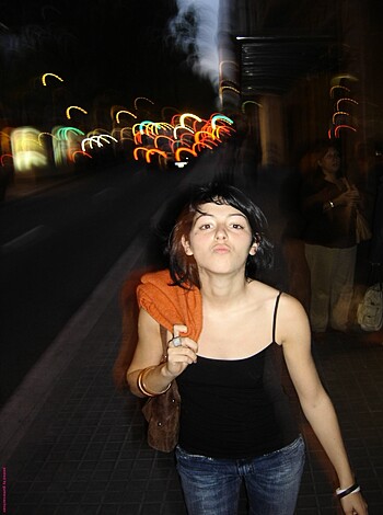 Here's a fuckin' picture of some bitch wearing a goddamn black top and jeans on some motherfuckin' city street at fuckin' night, sucking on her goddamn fingers while she gives a stupid kiss.