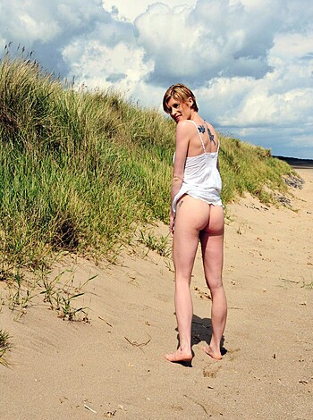 This photo shows a slender female ass and backside as she takes a stroll on the sandy beach while stark naked from the rear view.