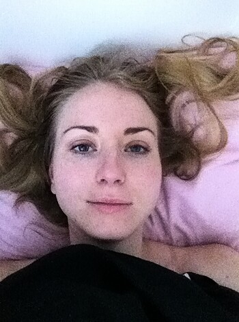 This image depicts a slender bitch who's spread her hair back while sporting a slight grin on her mug, donning black-assed PJs in the bedroom.