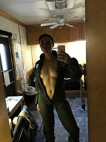A young blonde chick wears a tight-fitting, green flight suit with her ample boobs completely exposed, without any support from a bra.