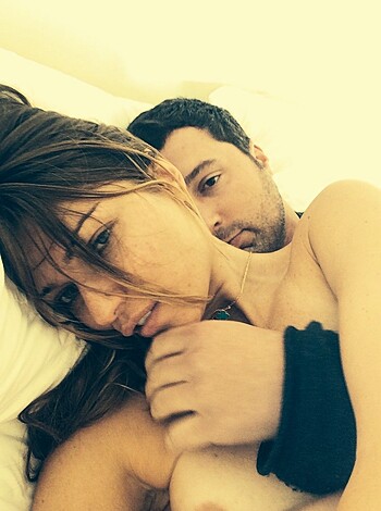 Here's a vulgar description of the image: "Fuckin' naked couple bonin' on a bed with the broad's head nestled on the dude's chest, suggestin' some serious fuckin' affection or possibly deep emotion."