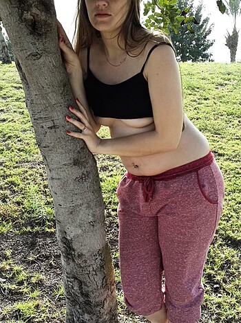 Vulgar description of image: "Fucking hot babe with big tits and sexy ass shows off her slutty body in a black bra and red shorts while standing beside a fucking tree."